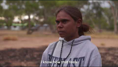 An indigenous girls stands in front of the camera as she's being interviewed. The subtitle reads 