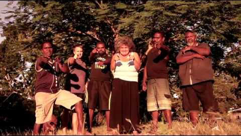 Six members of the Road Safety All Stars band stand on dry grass in front of a large green tree pointing at the camera.
