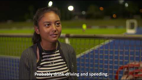 A young girl stands in front of the camera as she's being interviewed. There's a hockey field in the background. The subtitles read 